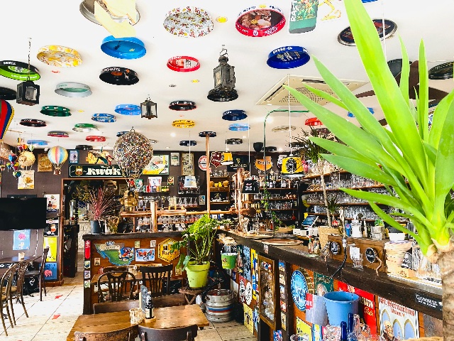 Vue intérieure d'un bar décoré de plateaux de bière au plafond et de plaques émaillées sur les comptoirs.