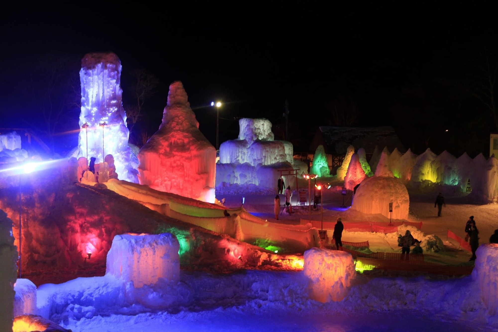 Grandes sculptures et structures de glace illuminées par des projecteurs multicolores la nuit.