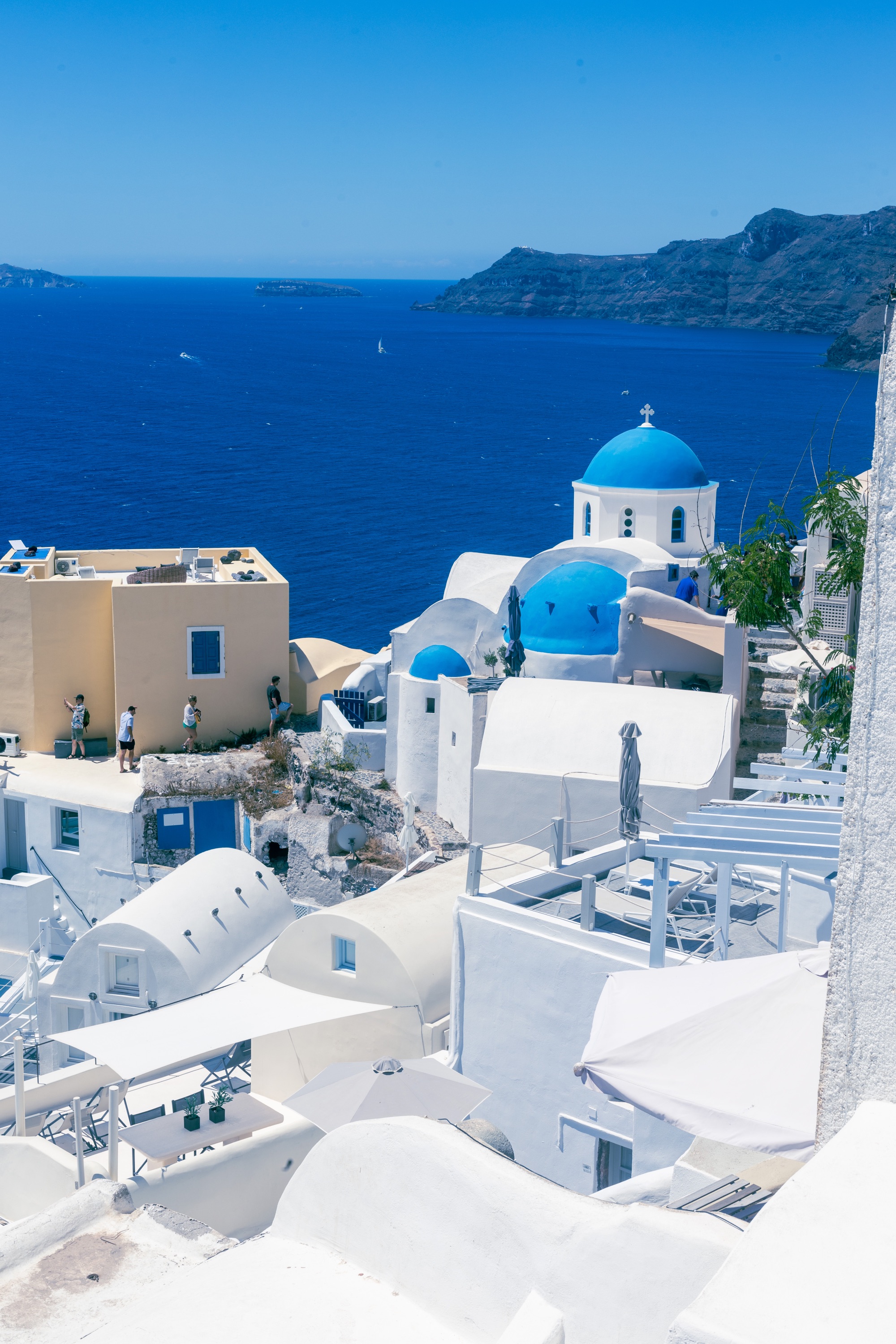 Vue plongeante sur les maisons blanches et les églises aux coupoles bleues d'Oia à Santorin, face à la mer Égée.