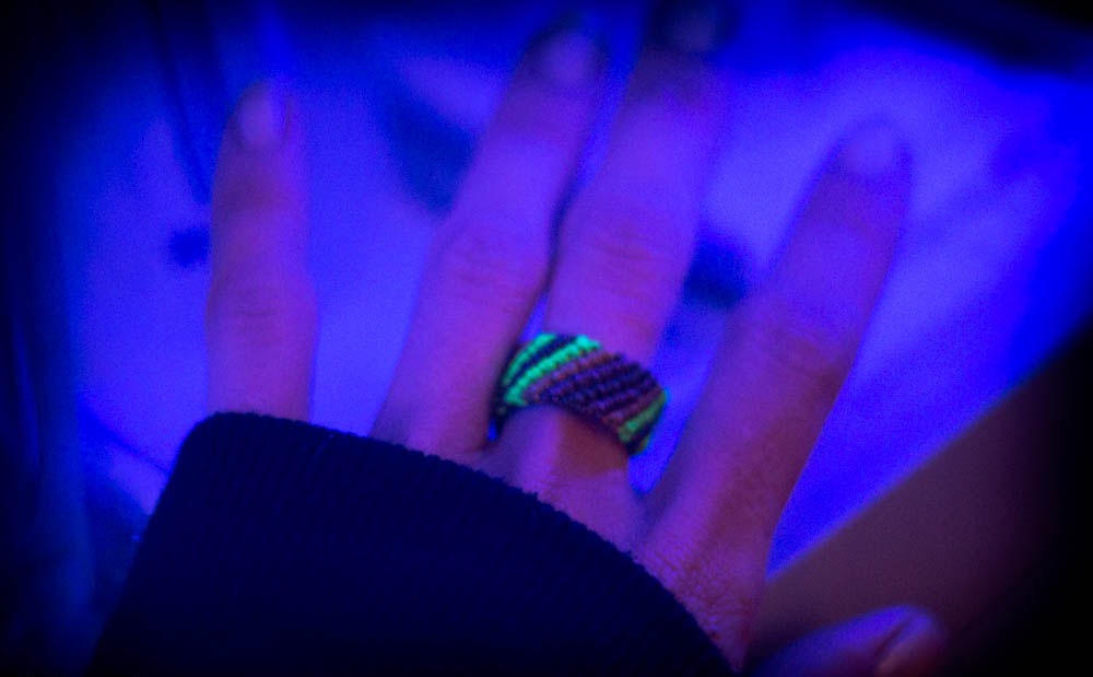 Gros plan sur une main portant une bague tissée fluorescente éclairée par une lumière bleue ultraviolette.