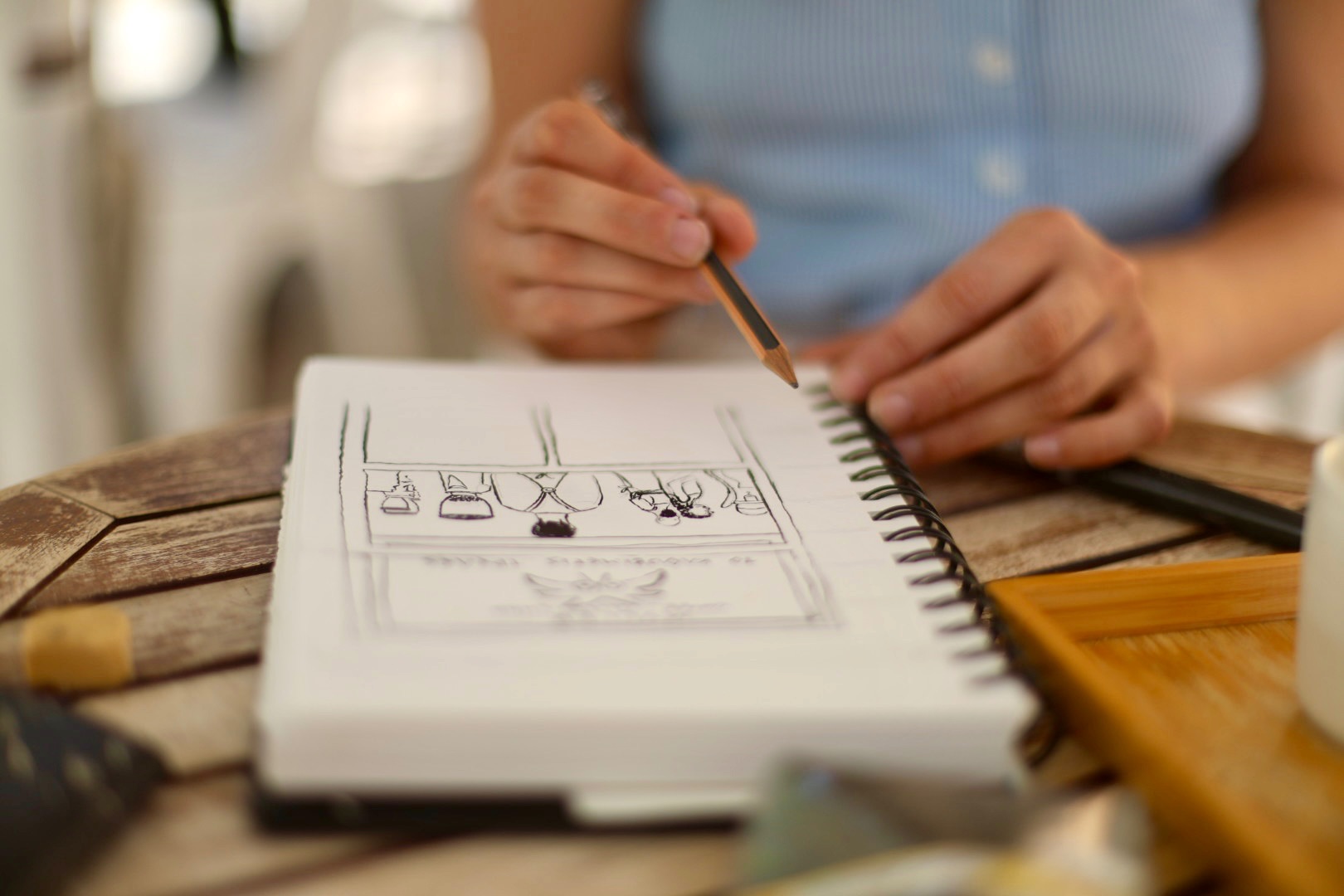 Gros plan sur les mains d'une personne dessinant au crayon dans un carnet à spirales sur une table en bois.