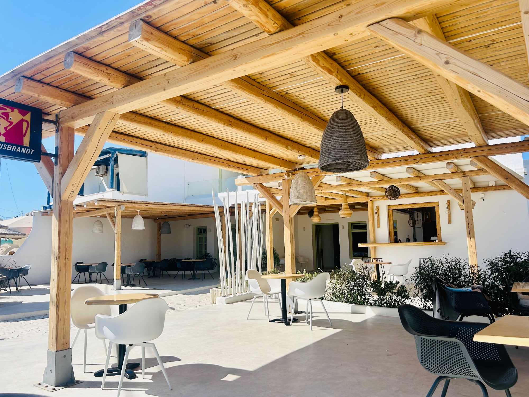 Terrasse extérieure d'un café avec pergola en bois, tables et chaises sous un ciel bleu.